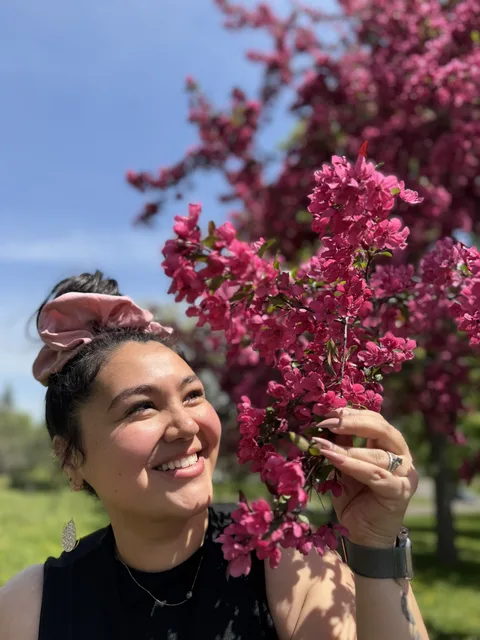 Alicia smiling beside vivid pink blossoms in spring